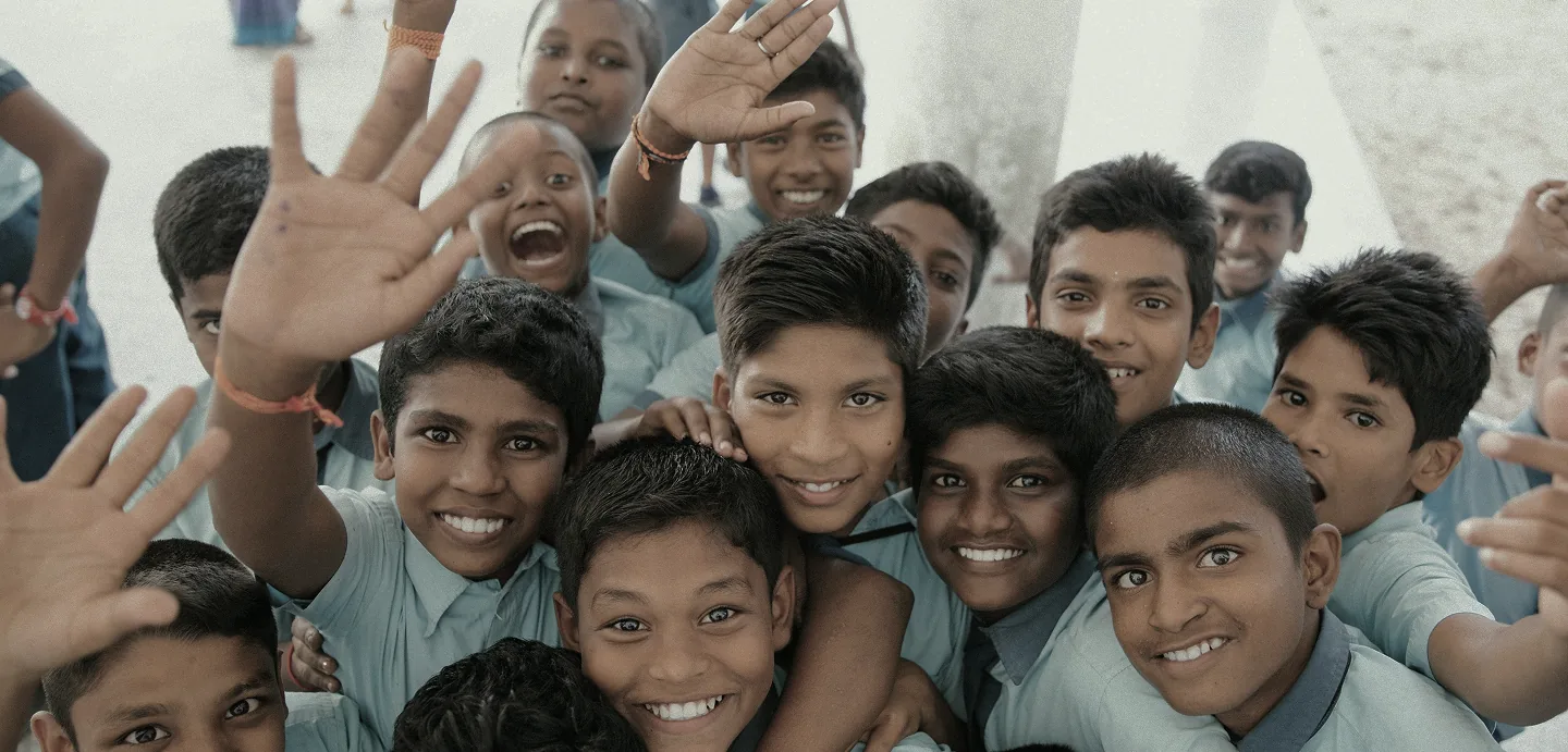 Schoolchildren waving and smiling inside a village classroom